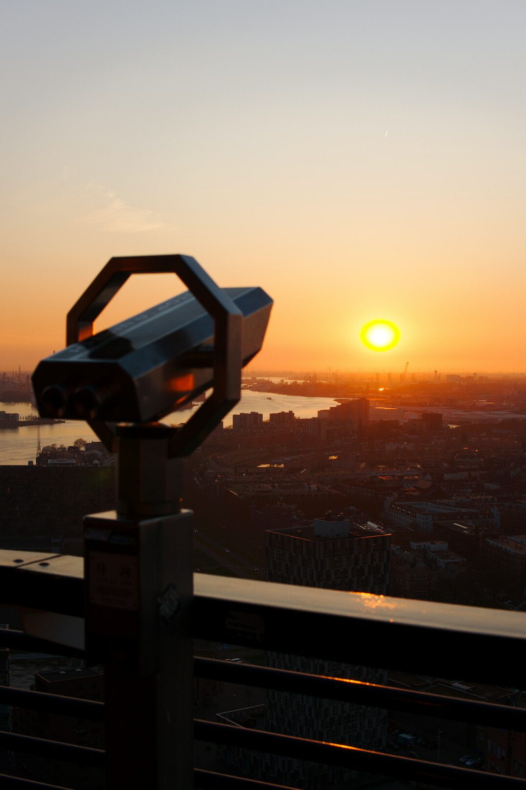 Video camera on a tripod silhouetted against a sunrise over a city